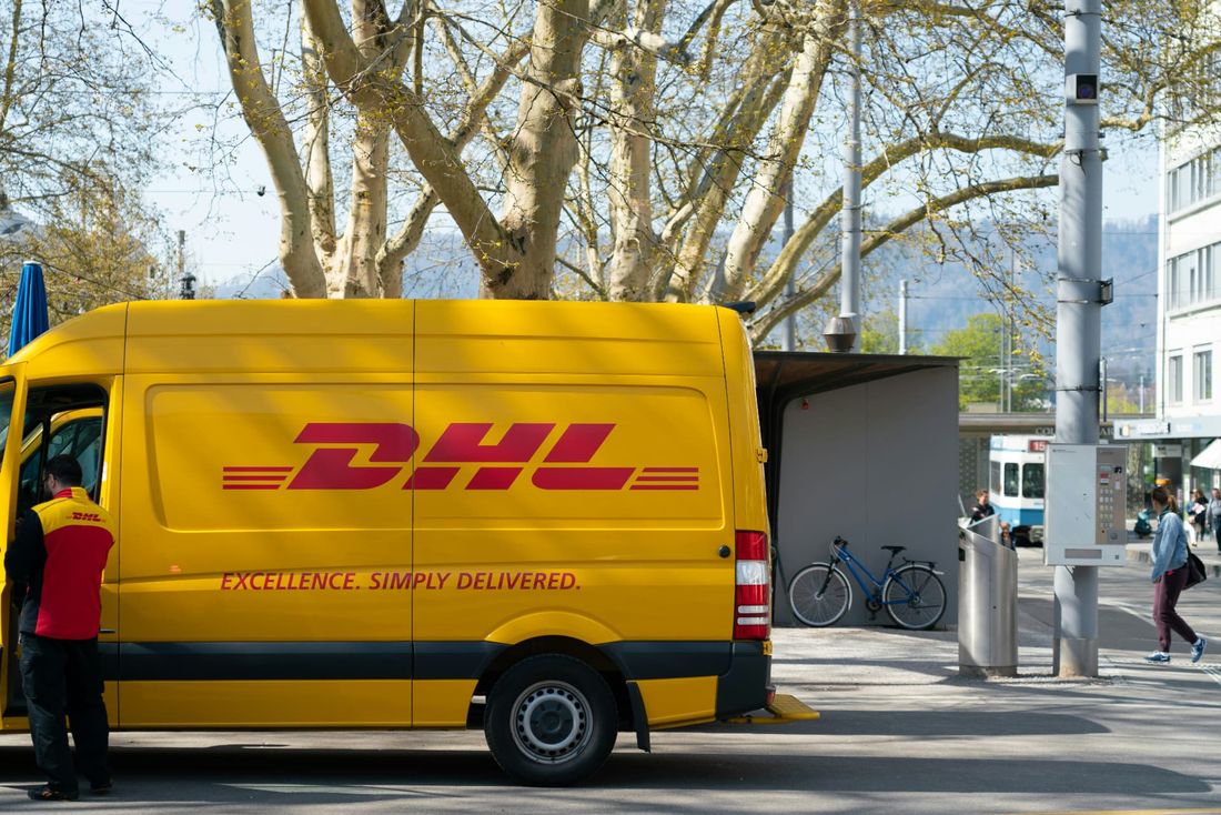Gelber DHL Transporter mit EXCELLENCE. SIMPLY DELIVERED. Schriftzug bei der Auslieferung in der Stadt